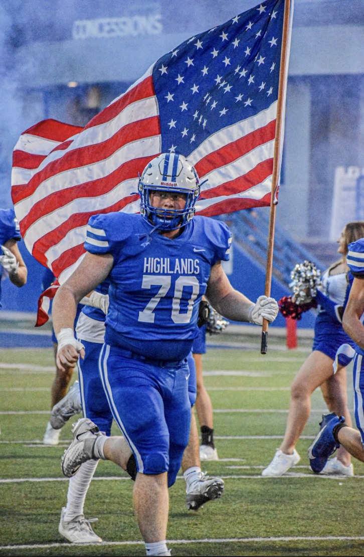 Torin Bryant (12) runs out onto the field holding the American flag.